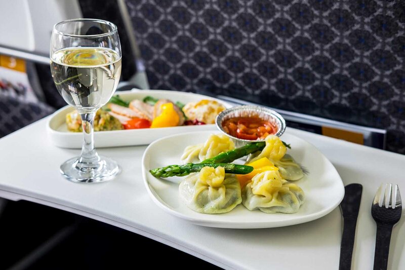 Plated dumplings topped with asparagus and seperate dish with chicken, vegetables and potato with a glass of white wine