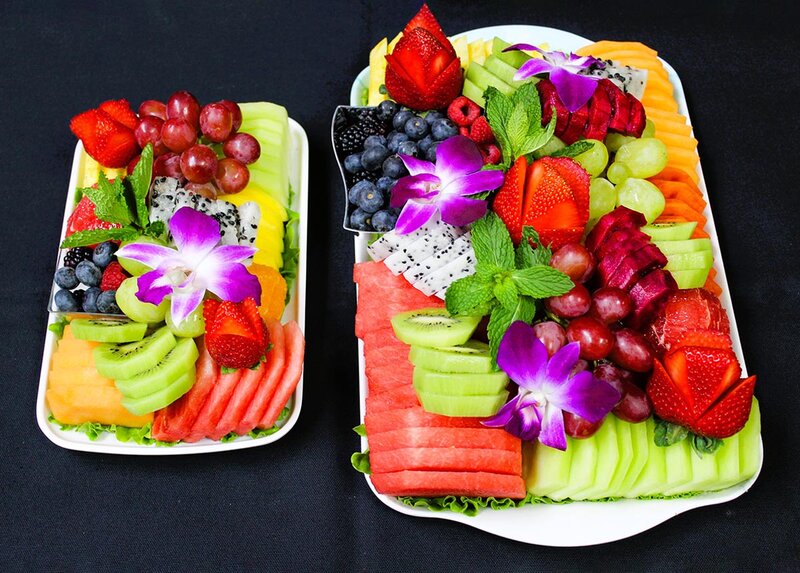 Two platters of fresh cut fruit topped with flowers